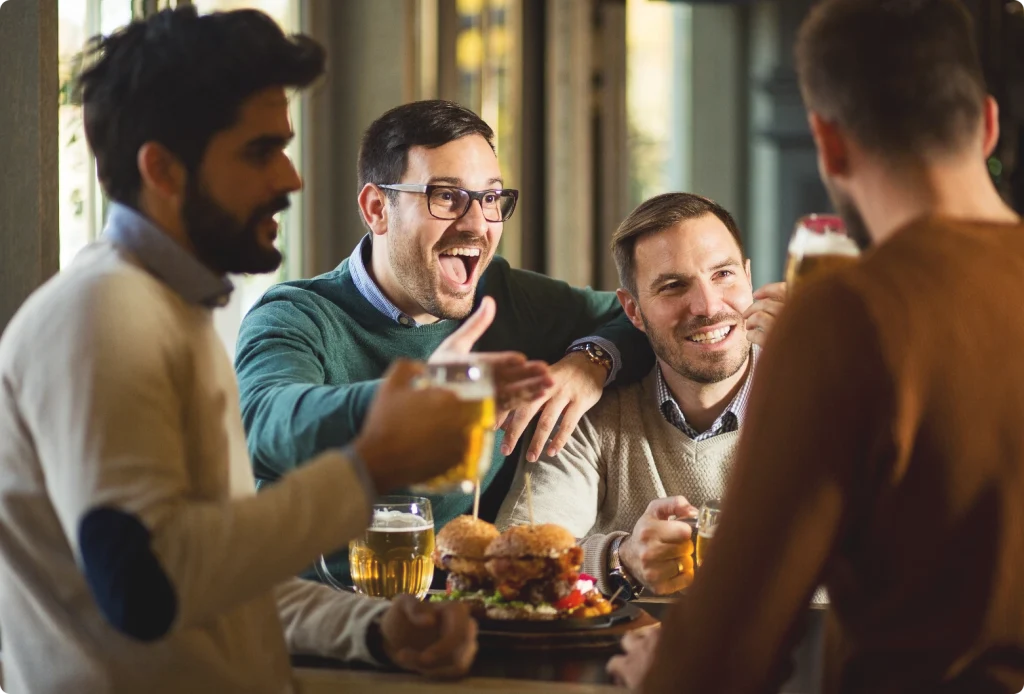 Män skrattar över öl och burgare i restaurangen