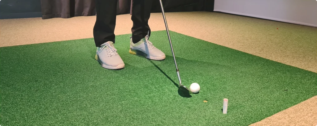 Golfsving på grön matta i simulatorn, bollen på väg mot duken